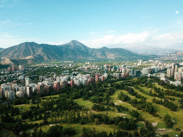 A golf course surrounded by a city beneath mountains.
