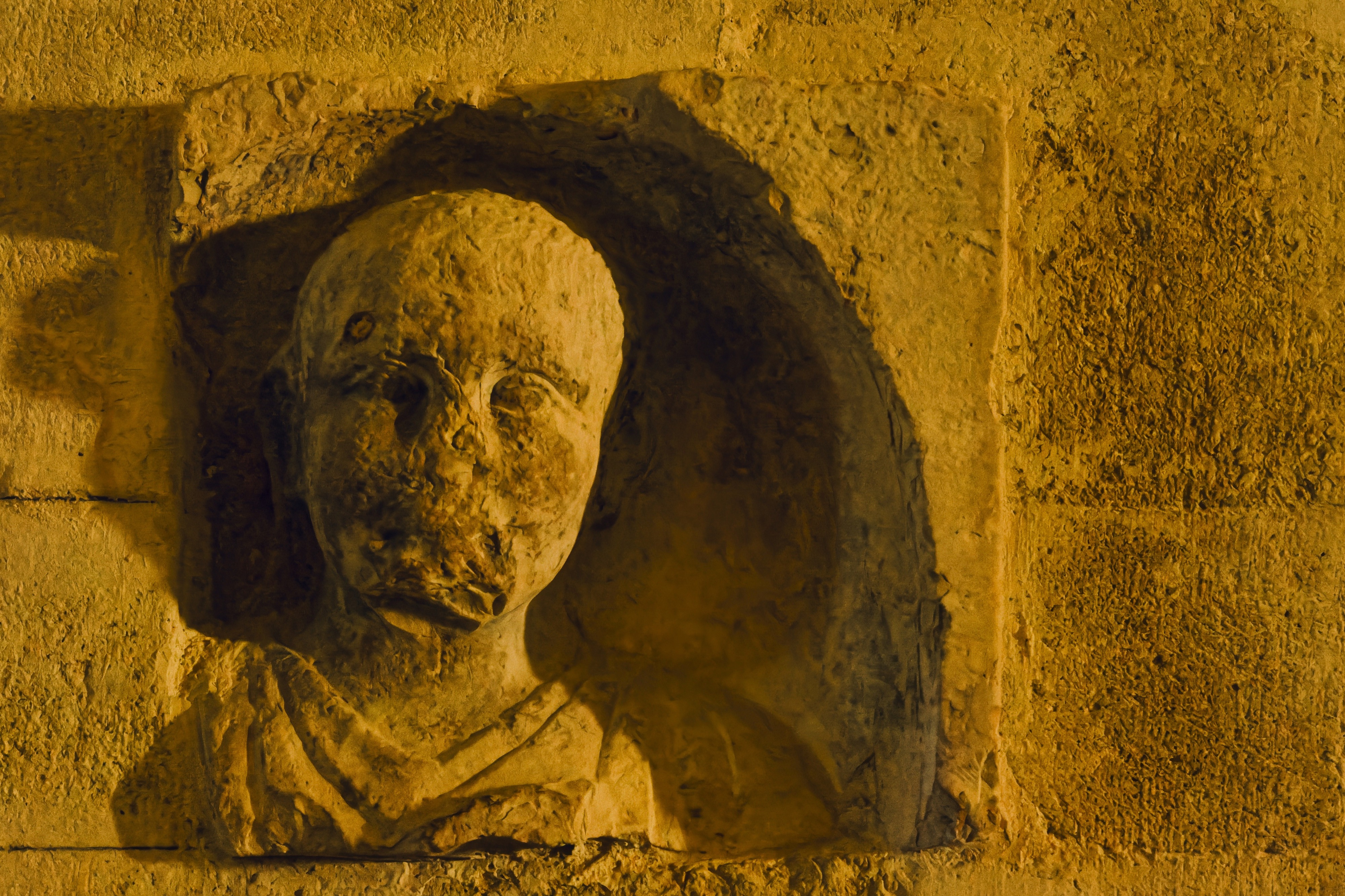 Ancient stone carving of a face displayed on a textured wall in a historical site during golden hour, Villeneuve-lès-Maguelone, France